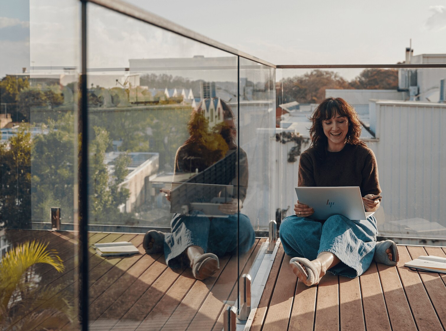 A woman sitting on the floor of her balcony working on an HP laptop on top of her lap.